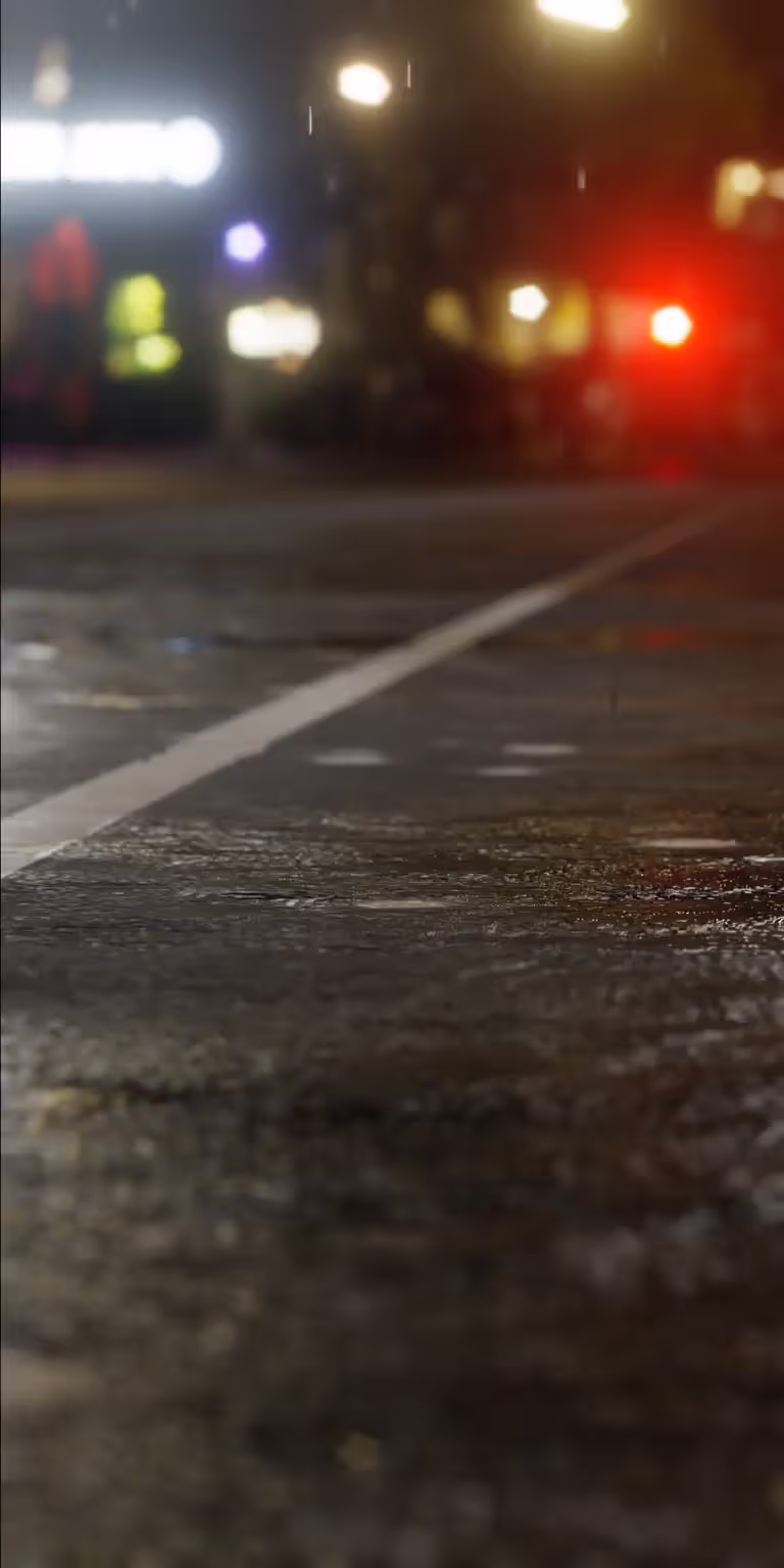 Rain falls on wet asphalt, creating ripples and reflections.